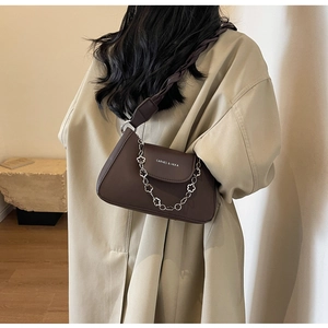 Detail of a dark brown leather crossbody bag featuring a floral silver chain and woven strap