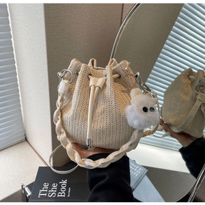 Detail of beige straw bucket bag with drawstring, wavy woven texture and cute plush charm
