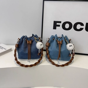 Denim drawstring bucket bag with woven leather handles and plush charm accessory