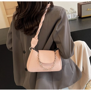 Detail of pink PU leather shoulder bag with twisted strap and silver flower chain on model