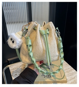 Close-up of woven straw bucket bag featuring a mint green drawstring and plush pom-pom