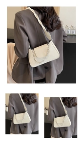 Detail of white leather shoulder bag featuring woven strap and silver ring chain accents