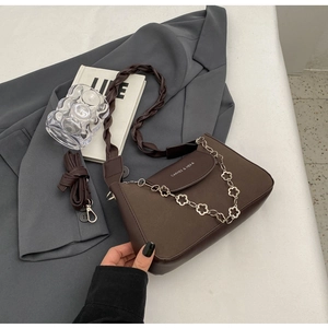 Detail of dark brown leather handbag with silver flower chain and woven strap over a blazer