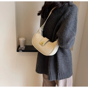 Détail du sac hobo en cuir beige avec boucle triangulaire dorée sur pull en maille
