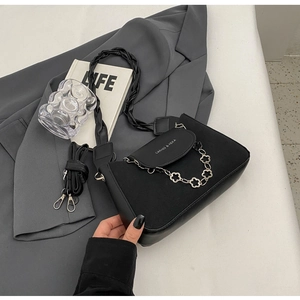 Close-up of black matte shoulder bag with silver floral chain and woven handle