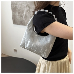 Detail of silver metallic pleated handbag featuring elegant large pearl handle decoration