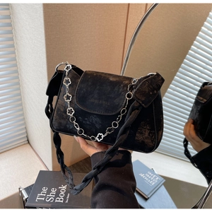 Close-up of black crossbody bag with vintage gold texture and floral chain strap detail
