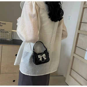 Détail du sac à paillettes noir avec nœud argenté et bandoulière chaîne porté par un mannequin
