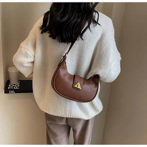 Détail d'un sac marron foncé avec grain litchi et fermoir triangle doré sur le modèle