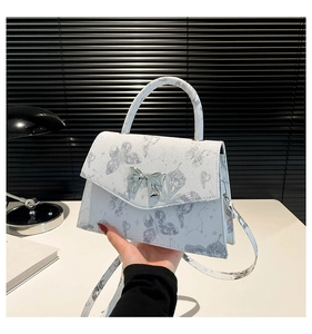 Détail du sac à main en cuir blanc avec imprimé papillon et boucle en nœud argenté