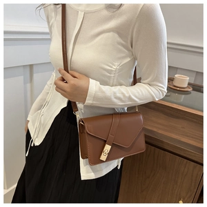Detail of caramel leather crossbody bag with gold lock worn with a white knit top