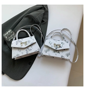 Détail d'un sac à bandoulière blanc avec imprimé papillon violet et fermoir nœud doré