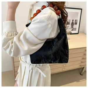Detail of black pleated cloud bag featuring oversized amber beaded chain handle