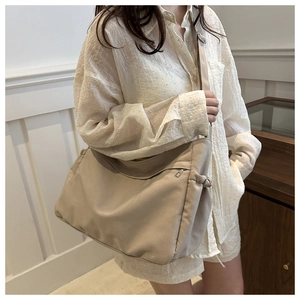 Close-up of beige nylon crossbody bag with drawstring side detail and metal zipper