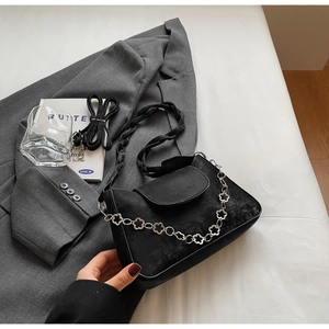 Close-up of black suede crossbody bag with decorative silver floral chain and woven handle