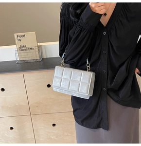 Detail of silver quilted crossbody bag with gold hardware worn by a model in black