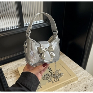 Détail de la texture à paillettes argentées et du nœud métallique sur le sac chic