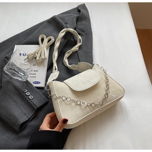 Detail of beige flap square bag with woven strap and silver flower chain on grey blazer