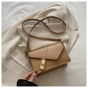 Detail of khaki leather crossbody bag with gold buckle lock on white blazer backdrop