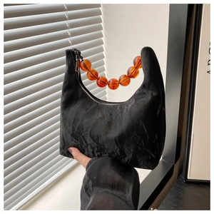 Detail of black crescent handbag featuring amber bead handle and pleated fabric texture