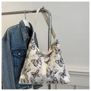 Detail of white canvas tote bag featuring black butterfly embroidery and feathered texture
