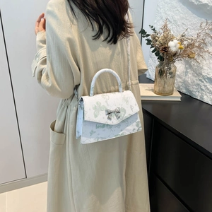 Sac bandoulière blanc élégant avec imprimé papillon vert et nœud argenté sur un manteau beige
