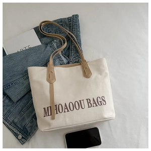 Mise à plat d'un sac cabas en toile crème avec lettrage marron à côté d'une veste en jean