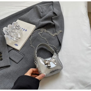 Détail d'un sac à main argenté à paillettes avec nœud métallique et bandoulière