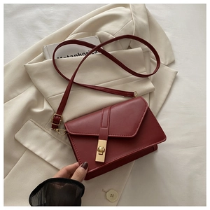 Detail of red leather crossbody bag featuring a long golden metallic lock on a white blazer