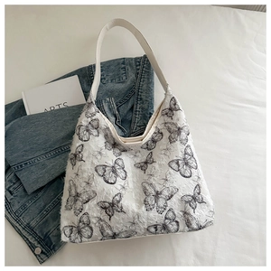 Detail of white canvas tote bag featuring black butterfly patterns and textured lace fabric