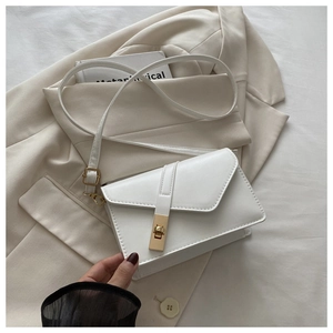 Detail of white PU leather crossbody bag with gold lock on a beige blazer background