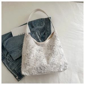 Detailed view of white canvas hobo bag with 3D lace butterfly embroidery and wide strap
