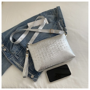 Close-up of silver crocodile pattern bag with dual straps on a casual bed setting