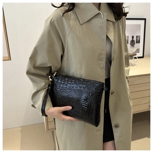 Detail of black crocodile texture envelope clutch bag with gold zipper and wrist strap