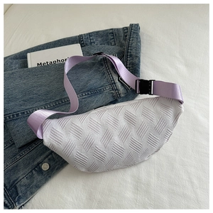 Detail of white woven crossbody bag with purple strap on denim and book backdrop