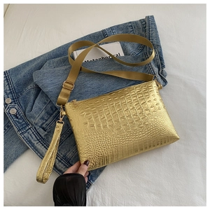 Detail view of metallic gold crocodile texture clutch with adjustable canvas strap