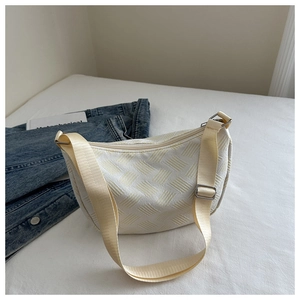 Close-up of cream textured crescent bag with adjustable strap and casual denim styling