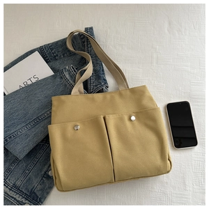 Detail of mustard yellow canvas tote bag with front pockets and silver snaps on a bed