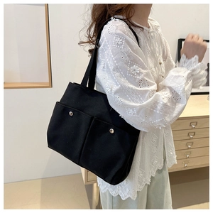 Detail of black canvas tote bag showing dual front pockets with silver buckles on shoulder