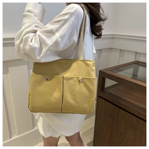 Detail of yellow canvas tote bag featuring large front pockets and silver metal buttons