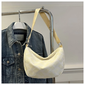 Close-up of beige woven texture underarm bag with wide nylon strap on denim jacket