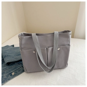 Detail of gray canvas tote bag featuring dual front pockets and silver metal button accents
