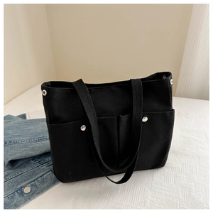 Detail of black canvas tote bag showing functional outer pockets and silver metal rivets