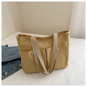 Detail of a yellow canvas tote bag with outer pockets and white woven shoulder strap