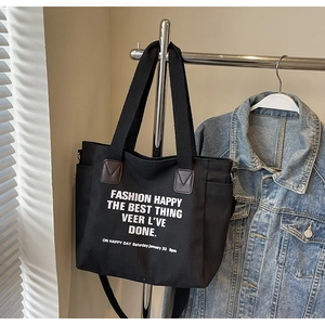 Détail du sac cabas en toile noire montrant la poche latérale et la poignée robuste