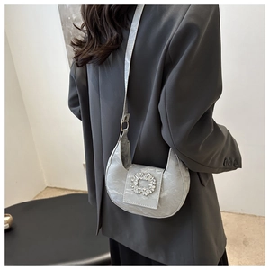 Grey half-moon crossbody bag with crystal buckle shown on model wearing a blazer