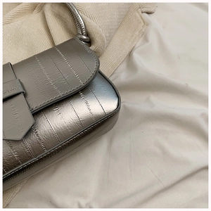 Detail of silver metallic shoulder bag with vertical pleats and a knotted strap design