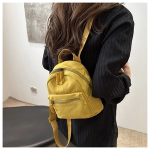 Close-up of yellow nylon mini backpack with adjustable straps worn on a black outfit