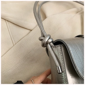 Close-up of metallic silver bag showing knotted shoulder strap and textured surface