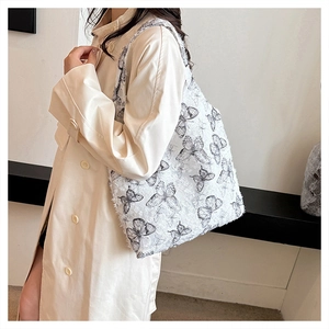 Detailed close-up of a white lace tote bag with black butterfly prints and fringed edges
